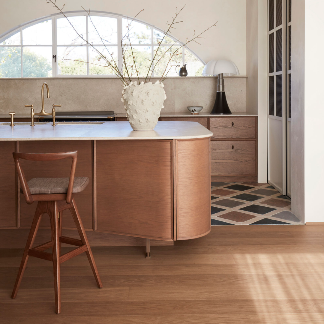 A modern kitchen island with a curved copper-toned wooden cabinet, a white countertop, and a TH Brown Danish Bar Stool in a bright, contemporary kitchen setting.
